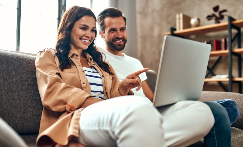 Happy couple on laptop searching homes for sale 